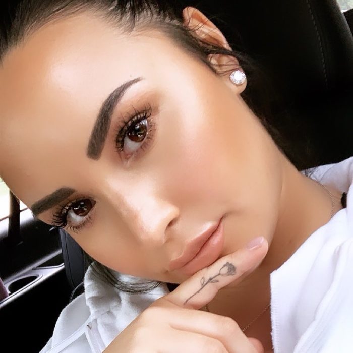 Demi Lovato mostrando su tatuaje de rosa en el dedo mñique