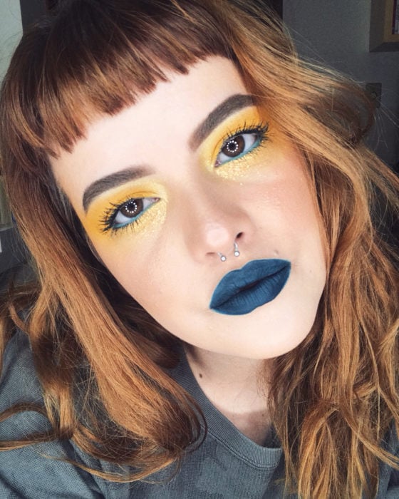 Modelo con maquillaje con sombras metalizadas en tono amarillo y labial azul oscuro