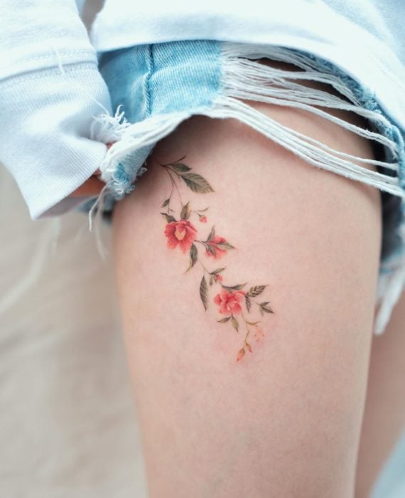 Tatuaje flores tonos cálidos en muslo