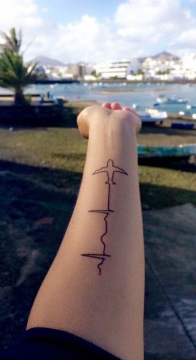 Chica mostrando su antebrazo con tatuaje de una silueta de avión y línea de electrocardiograma