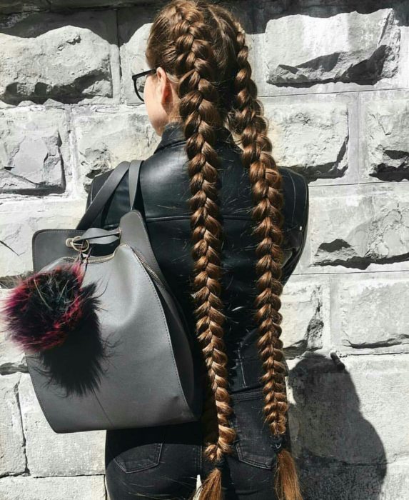 Chica de chamarra de piel negra, con mochila gris, peinada con trenzas holandesas de cabello largo