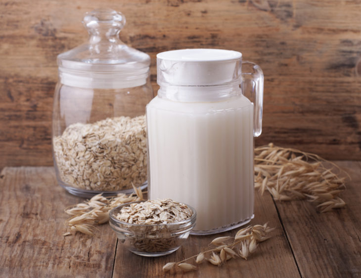 Agua de avena en jarra y jarrón y tazón con hojuelas de avena sobre mesa de madera