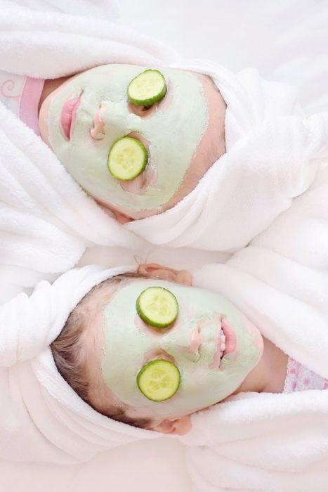 Par de amigas con mascarilla en el rostro y rodajas de pepino sobre los ojos