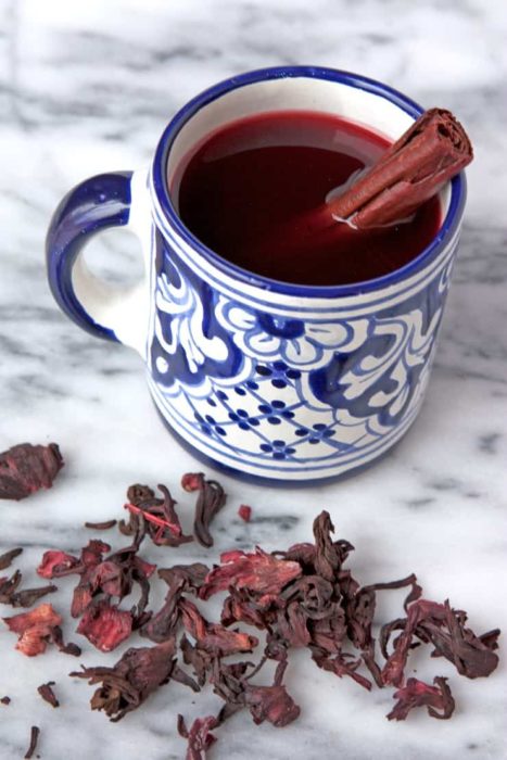 Té de canela en taza adornada, con jamaica sobre mesa de marmol