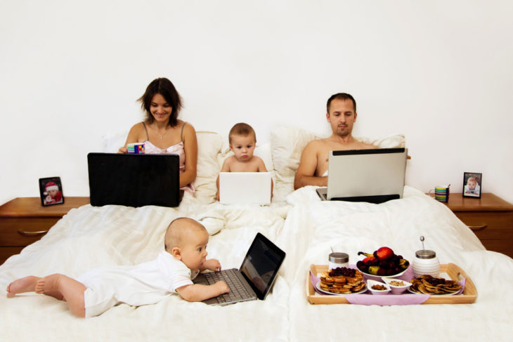 Familia recorstada en la cama usando laptops