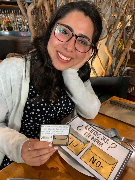 Chica sacando una nota de una invitación a un concierto y sonriendo en un restaurante