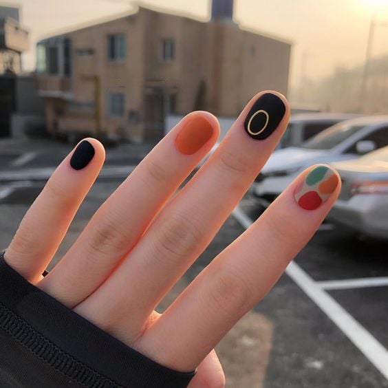 Manicura en uñas cortas con tonos negro, naranja y de colores neutros