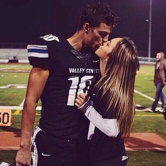 Pareja en un partido de futbol americano dándose un beso 