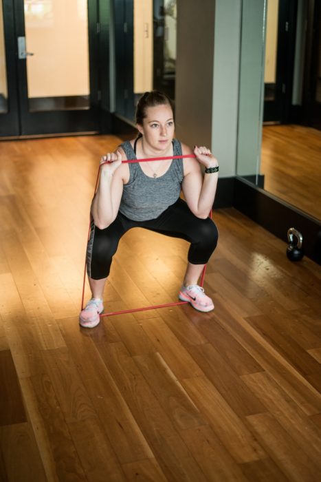 Chica haciendo sentadillas con liga y ropa deportiva