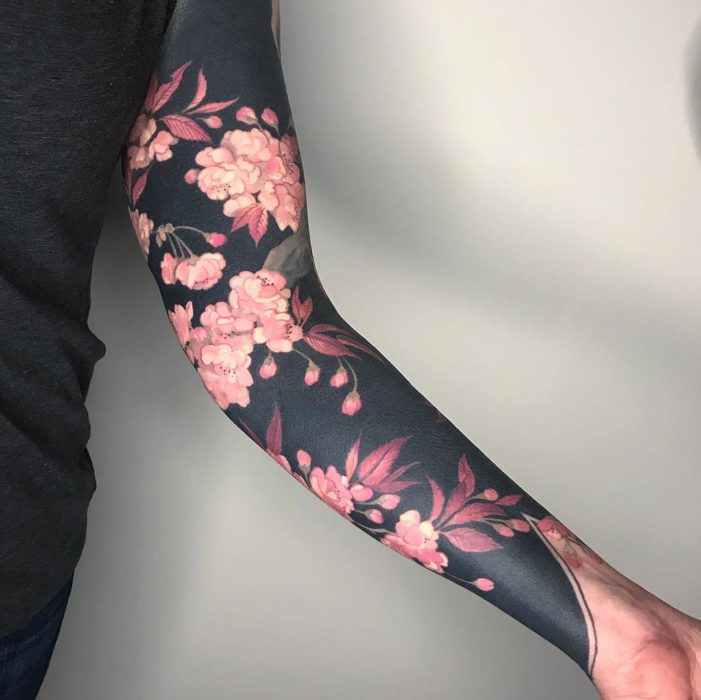 Tatuaje tipo manga con fondo negro y flores rosadas