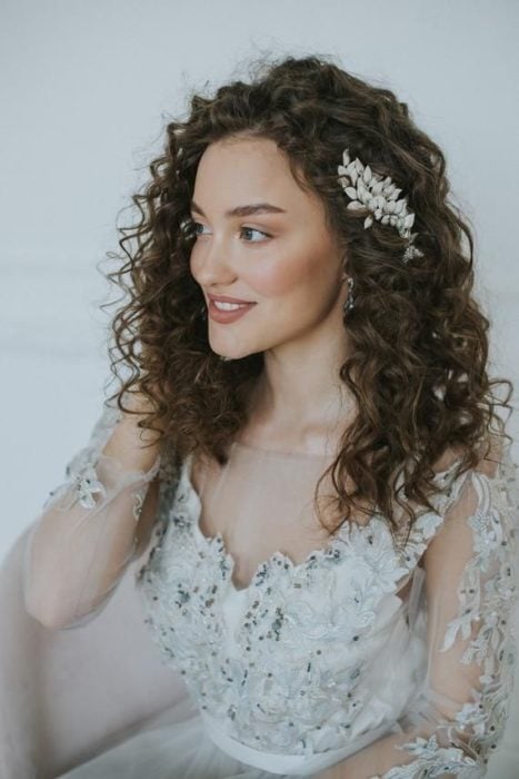 Peinado de novia de cabello rizado usando el tocado de lado