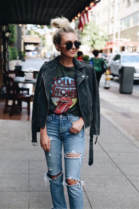 Chica posando para una foto mientras usa jeans rasgados, una camisa negra y chaqueta de cuero