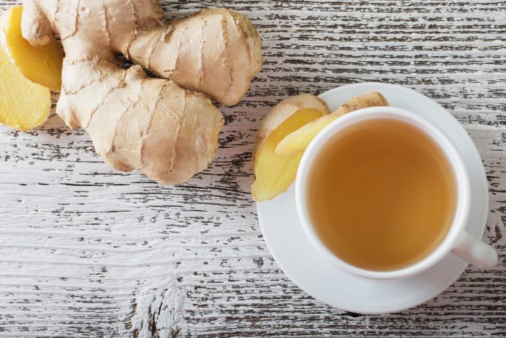 Té de jengibre en taza blanca, sobre mesa de madera blanca desgastada