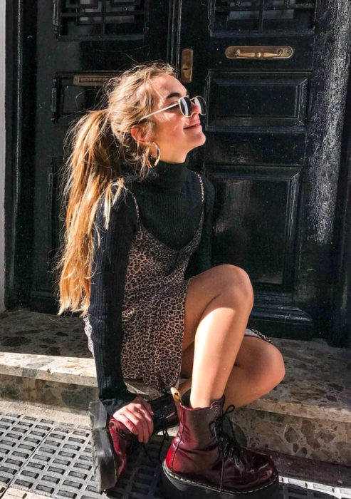 Looks con vestidos y blusas básicas; chica sentada en pórtico, peinado de coleta de caballo despeinada, lentes de sol, vestido de animal print con encaje, botas Dr. Martens color vino, suéter negro con cuello de tortuga