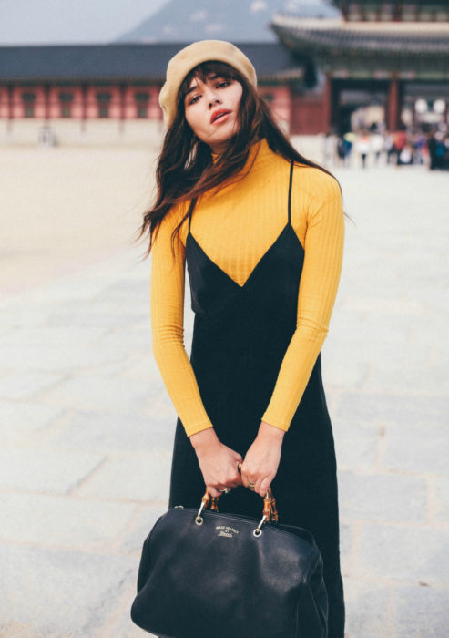 Looks con vestidos y blusas básicas; mujer con vestido negro, blusa amarilla de manga larga, boina francesa