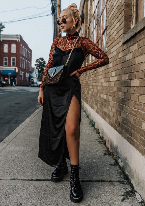 Looks con vestidos y blusas básicas; mujer en la calle, cabello rubio peinado de chongo despeinado, con lentes de sol, blusa de animal print de manga larga y cuello alto, vestido largo y negro de satín, botas Dr. Martens de plataforma