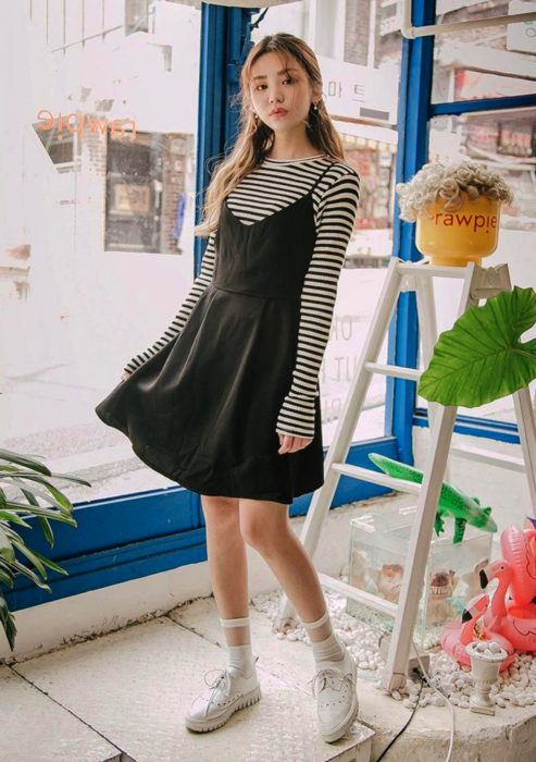 Looks con vestidos y blusas básicas; mujer coreana con vestido sencillo negro, blusa rayada, tenis blancos y peinado de media coleta