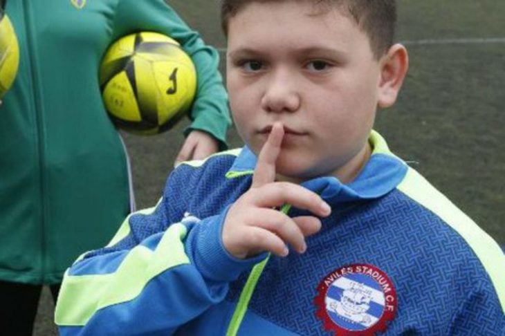 Niño haciendo señal de silencio con el dedo en un estadio de fútbol 