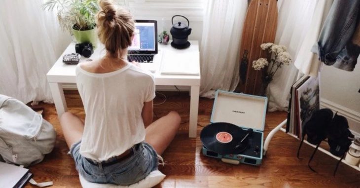 Chica sentada frente al computador escuchando música con un tocadiscos