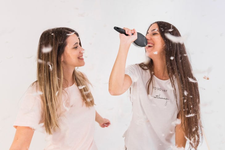Amigas simulando cantar karaoke con un cepillo para cabello