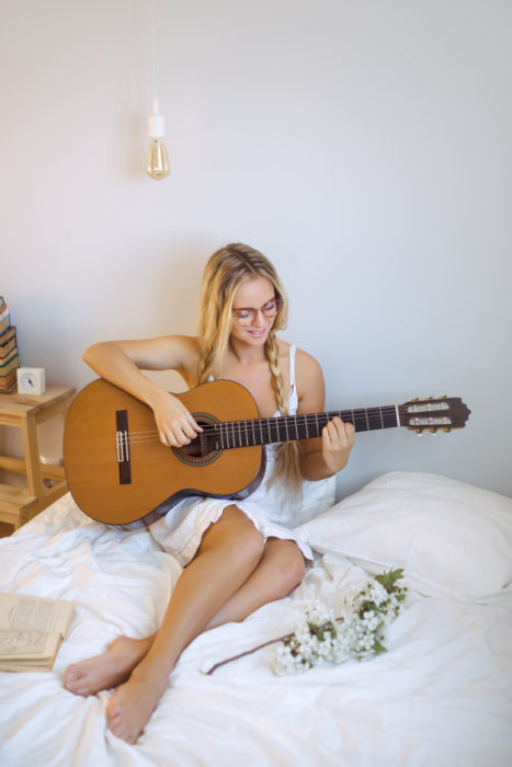 Chica tocando la guitarra recostada en una cama