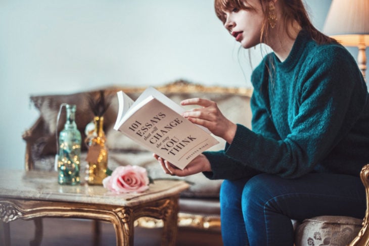 Chica leyendo un libro sentada en un sofá de madera con detalles dorados