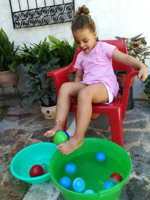 Niña juega a sacar pelotitas del agua con sus pies