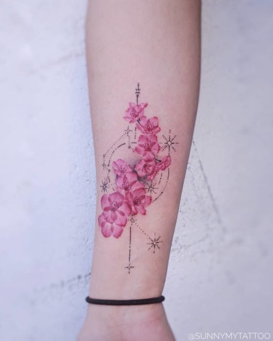 Tatuaje de la constelación de acuario adornada con flores del árbol de cerezo en el área del antebrazo