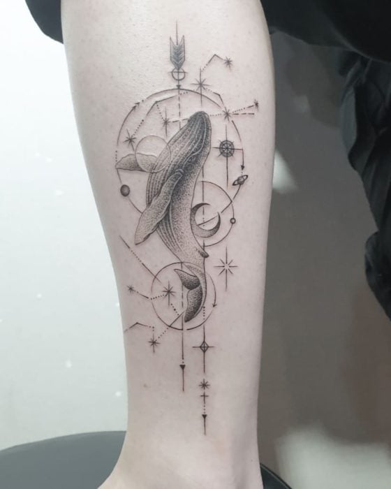 Tatuaje de la constelación de acuario con una ballena sobre ella y otros detalles a tinta negra en el área del antebrazo