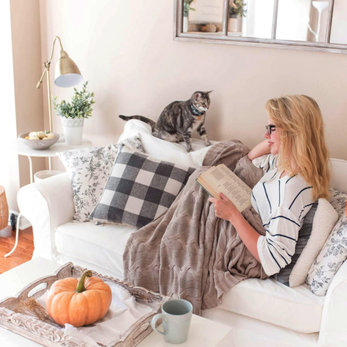 Mujer rubia leyendo libro en el sillón con su gato