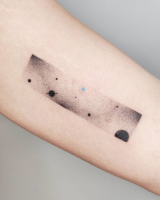Tatuaje al estilo hand poke de una galaxia con planetas y estrellas