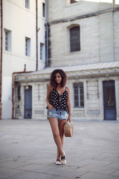 Mujer con bob largo posa en la calle con blusa negra con puntos blancos, short y bailarinas beige