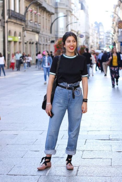 Chica sonríe y viste jeans azules con blusa negra y bailarinas rosas con lazos negros 