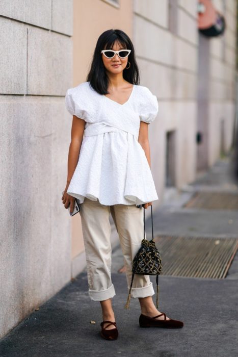 Mujer con blusa larga blanca y pescadores beige posa con sus bailarinas borgoña de terciopelo