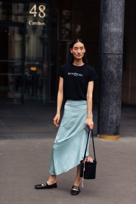 Mujer asiática con cabello recogido posa con falsa azul, blusa negra y bailarinas negras