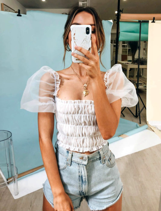 Mujer tomándose selfie frente al espejo con top blanco de mangas gigot y short