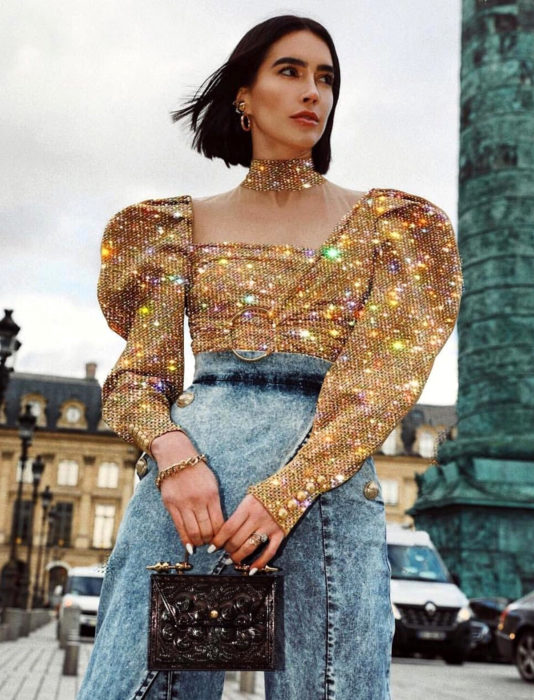 Mujer de cabello corto de hongo, con blusa dorada con brillo y mangas gigot, mom jean a la cintura