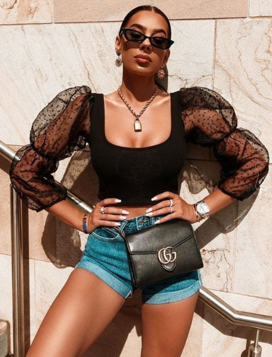 Chica morena tomando el sol, lentes oscuros, top negro con mangas gigot de encaje y short