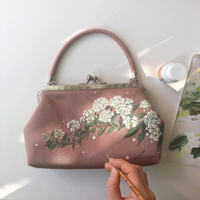 Bolsa de mano color rosa palo con hojas verdes y flores pequeñas blancas