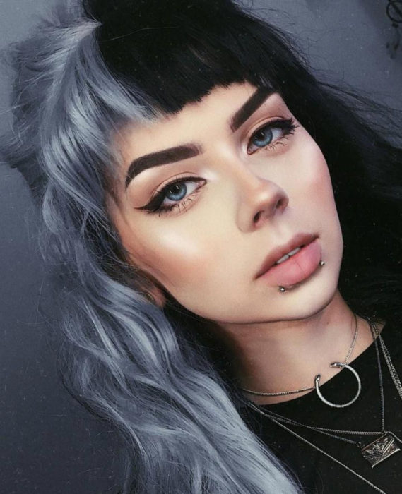 Cabello negro con blanco; chica de ojos azules con maquillaje natural, piercings en el labio, tinte bicolor, oscuro y gris, copete disparejo