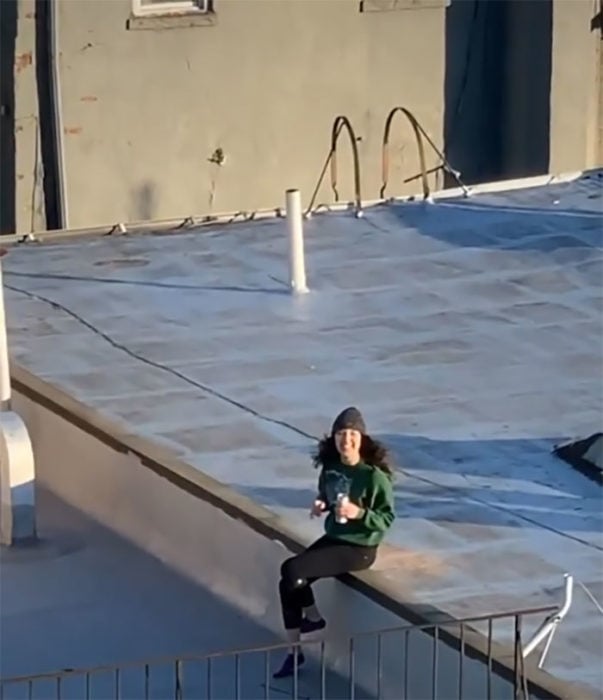 Chica sentada en el techo de su casa recibiendo un dron de un chico
