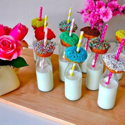 vasos de vidrio con leche y donas de colores como refrigerio para fiesta infantil