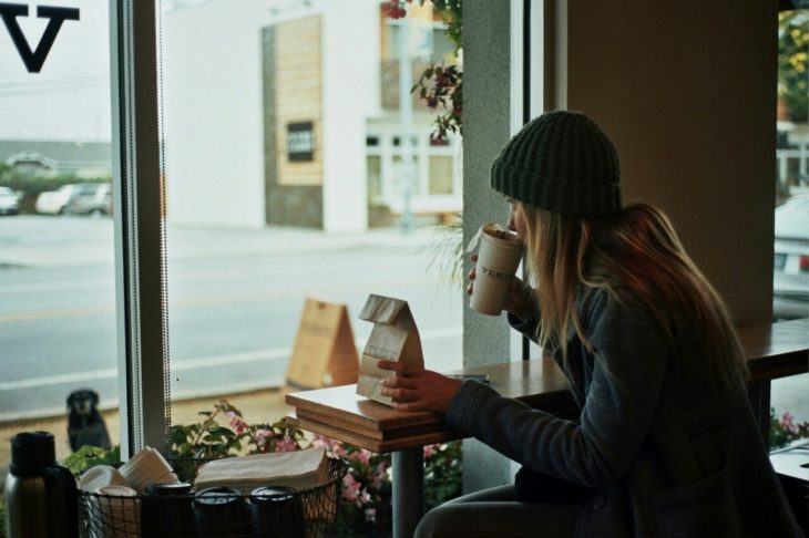 Chica rubia toma café mientras por la ventana de una caftería