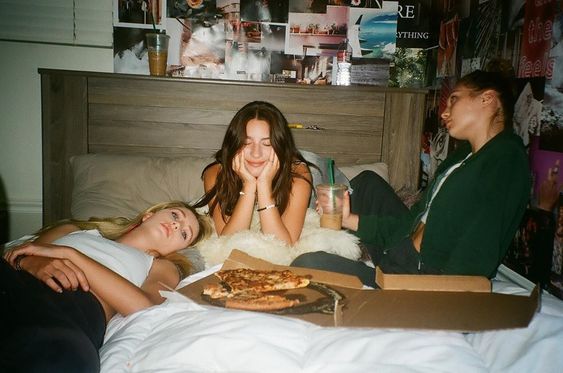 Tres amigas acostadas en la cama comiendo pizza