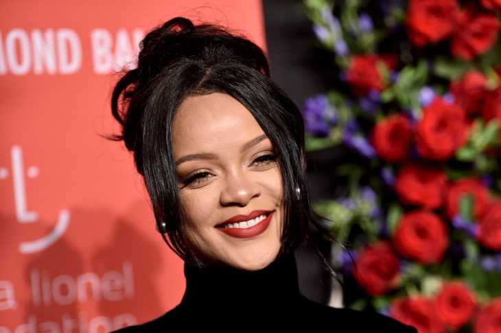 Rihanna sonriendo ligeramente e una alfombra roja son rosas