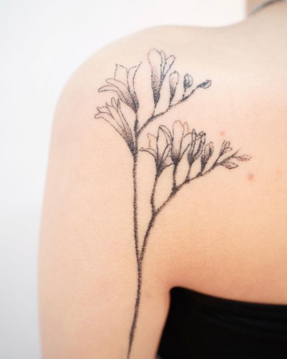 Tatuaje al estilo hand poke de flores y botones de flores abriéndose en el área del omóplato 