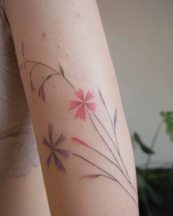 Tatuaje al estilo hand poke de flores de colores en el área del brazo