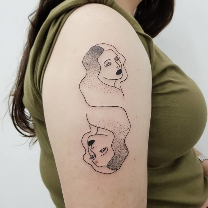 Tatuaje de geminis en tinta negra en la parte externa del brazo