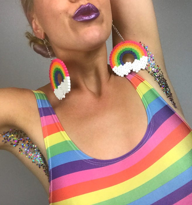 Glitterpits la nueva moda de Instagram en la que mujeres ponen diamantina en sus axilas; mujer con blusa de colores y aretes de arcoíris 