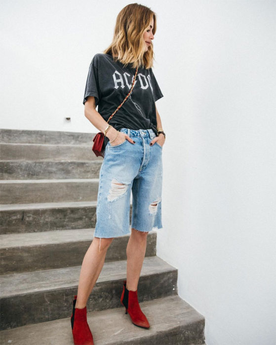 Chica usando bermudas de mezclilla con camisa rockera de color negro con botines de color rojo 